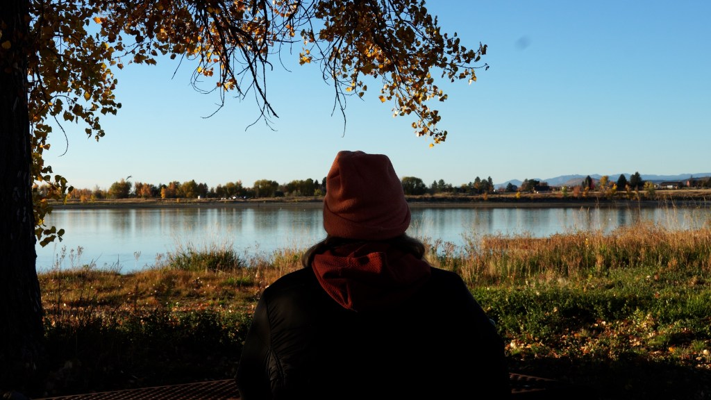 Person sitting by a calm water reservoir under autumn foliage, enjoying a peaceful morning view.